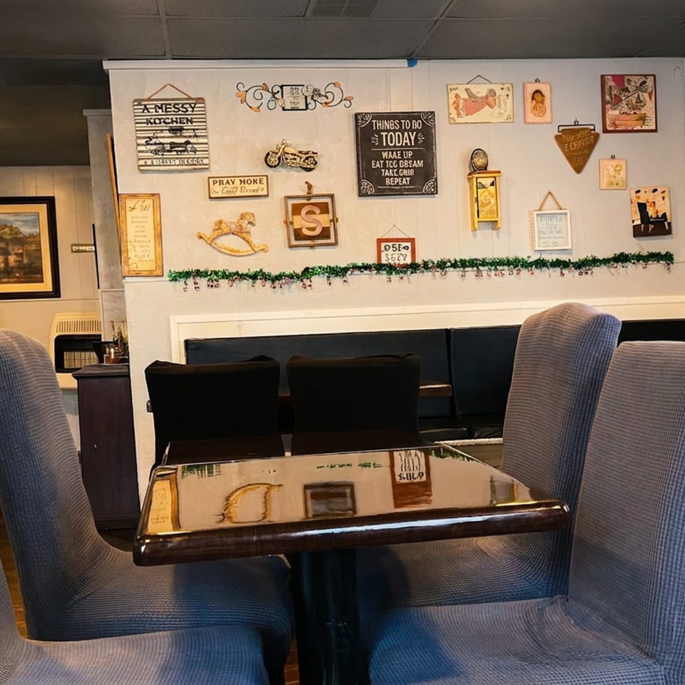 Cozy restaurant interior with upholstered chairs, dark tables, and decorative wall art including a "WELCOME" sign.