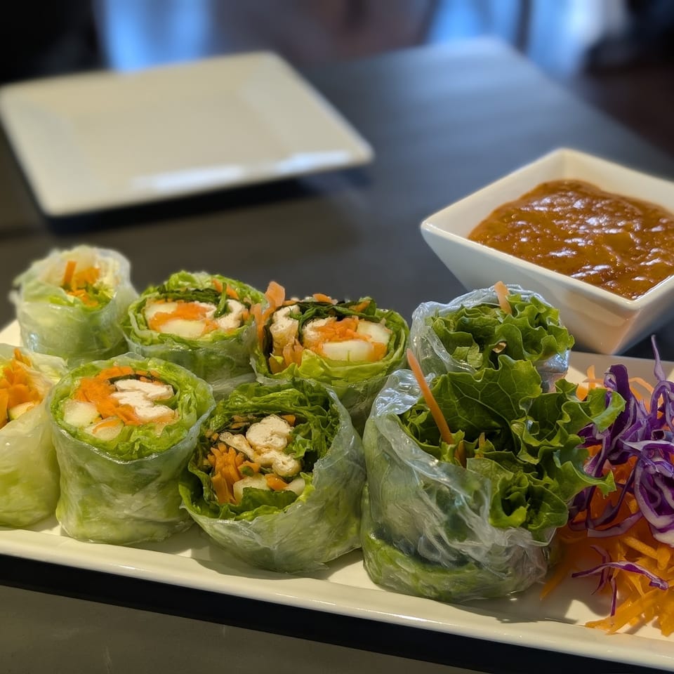 Fresh spring rolls with chicken, lettuce, and carrots, served with peanut sauce and shredded vegetables.