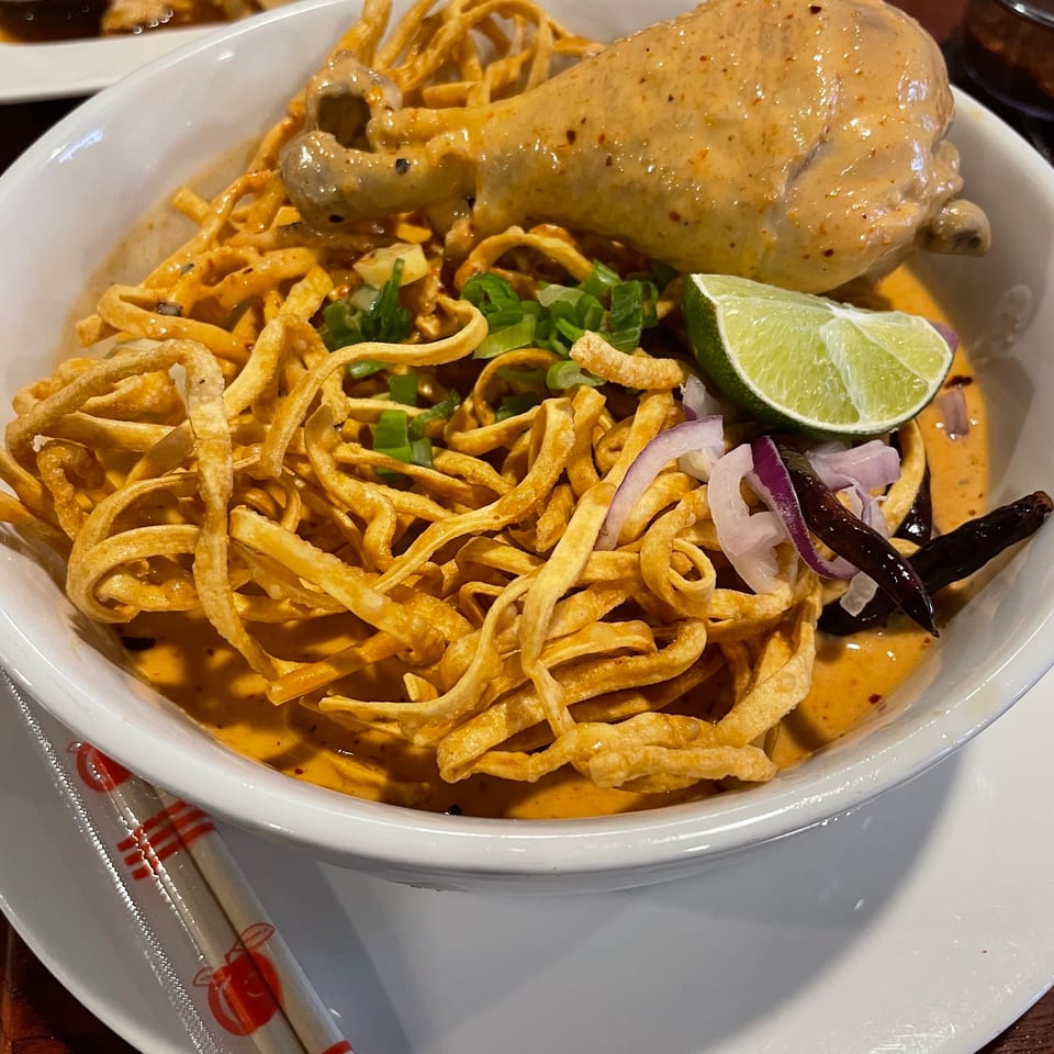 Close-up of a bowl of Khao Soi with chicken, crispy noodles, lime, and red onion.
