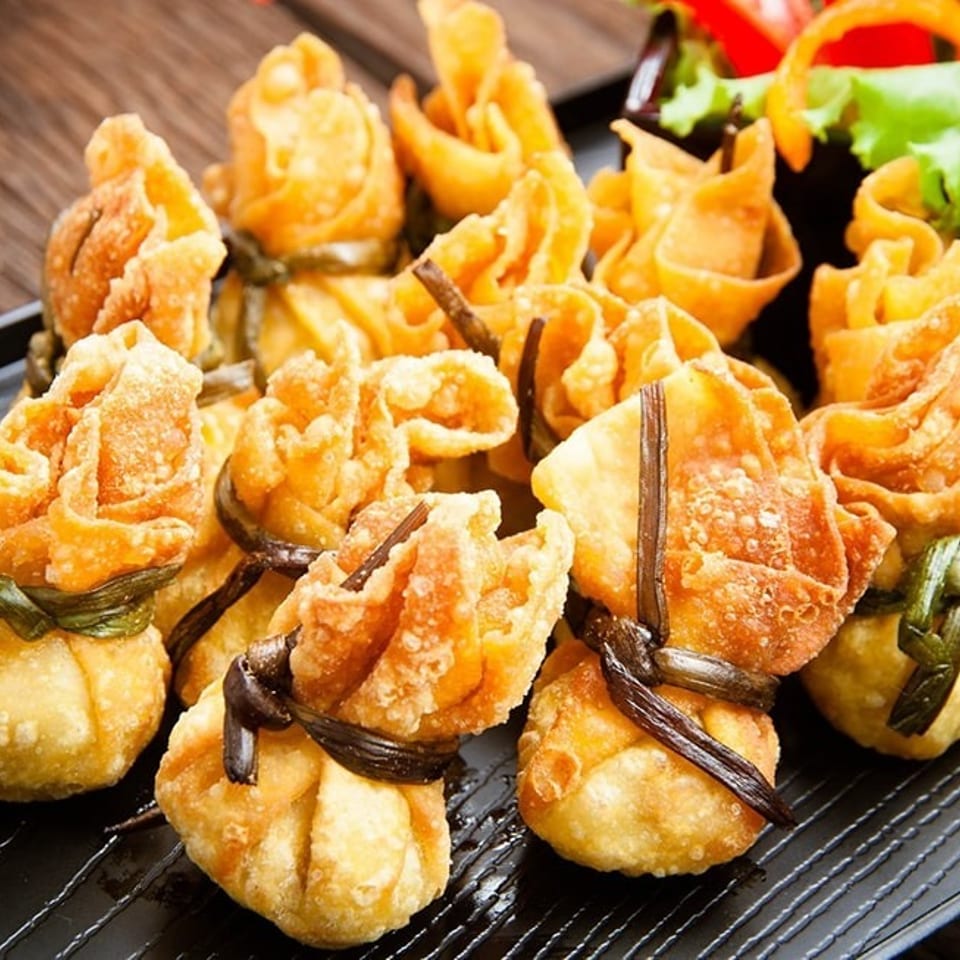 Golden fried wonton purses, tied with green and brown string, on a black rectangular plate.
