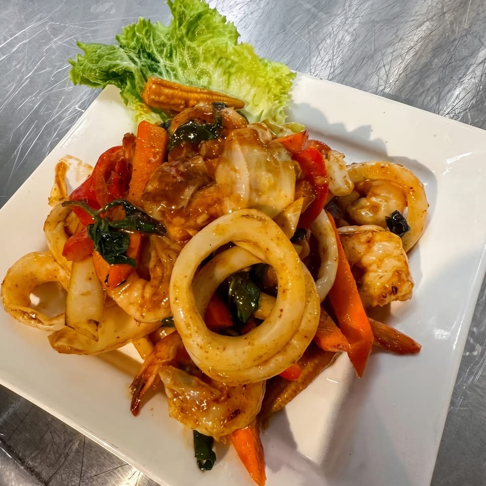 Stir-fried seafood with squid, shrimp, and vegetables in a savory sauce, garnished with lettuce.