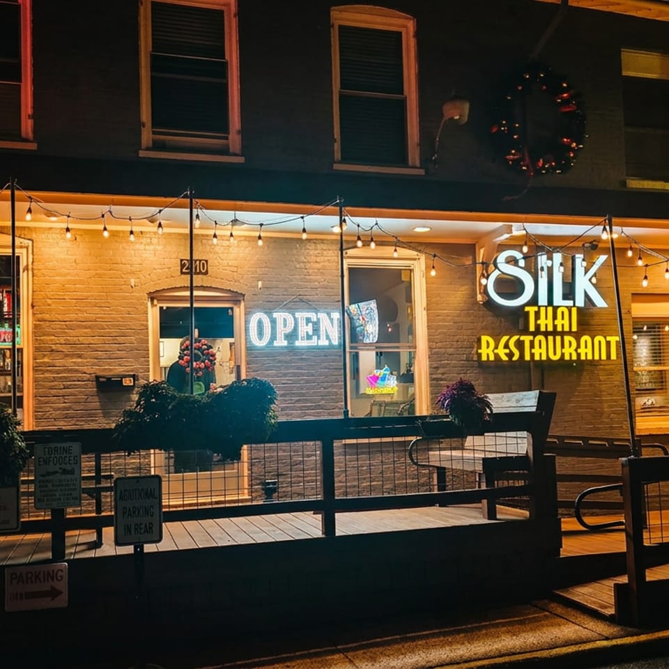 Exterior of Silk Thai Restaurant at night, with an "OPEN" sign and string lights illuminating the facade.