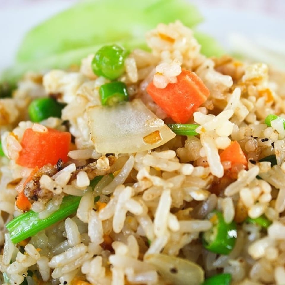 Close-up of fried rice with carrots, peas, onions, and green beans, garnished with lime and scallions.