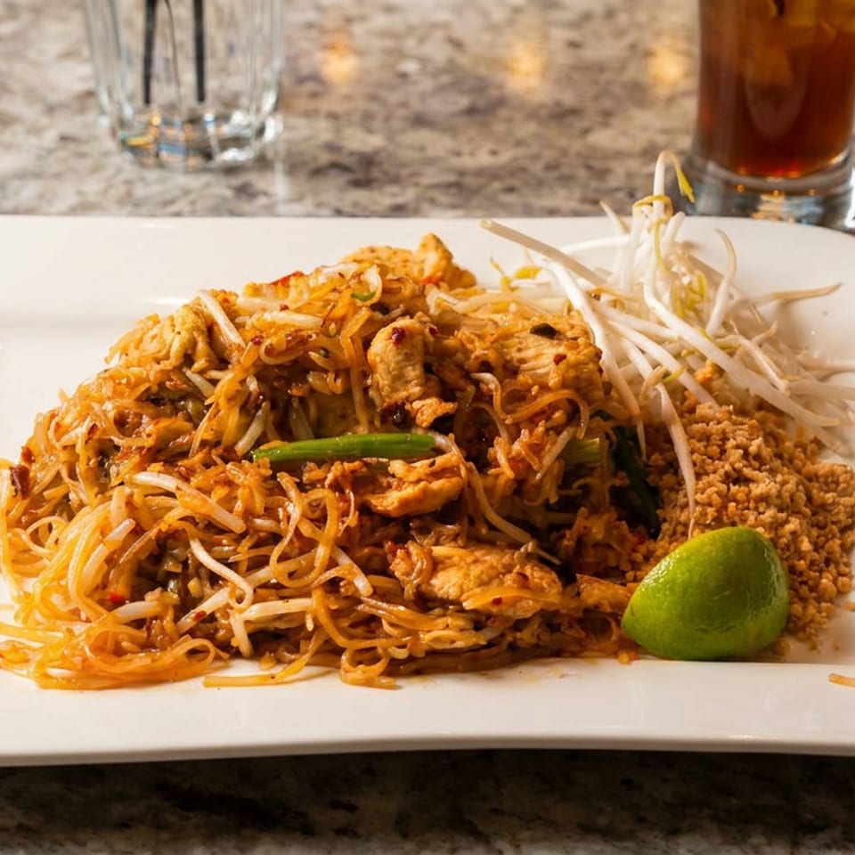 A plate of chicken pad thai with bean sprouts, crushed peanuts, and a lime wedge.
