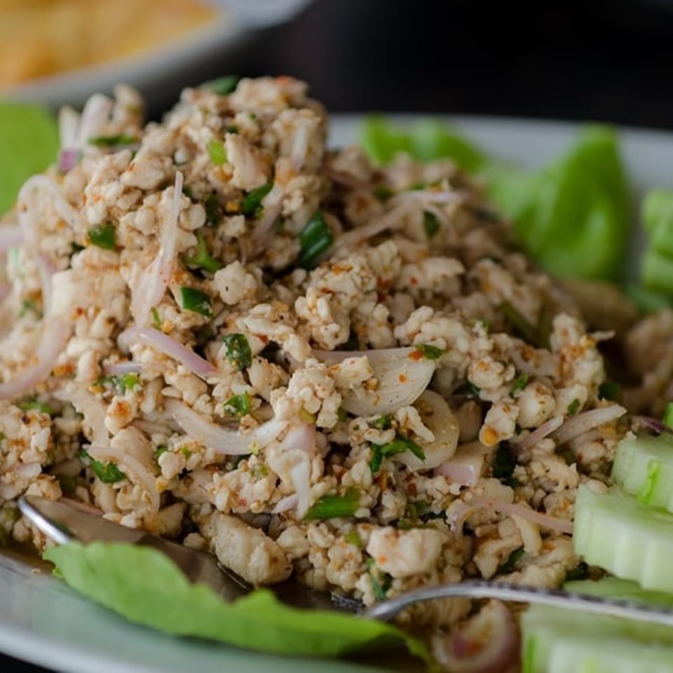 Spicy minced chicken salad (larb gai) with red onions, green herbs, and cucumber slices on lettuce.
